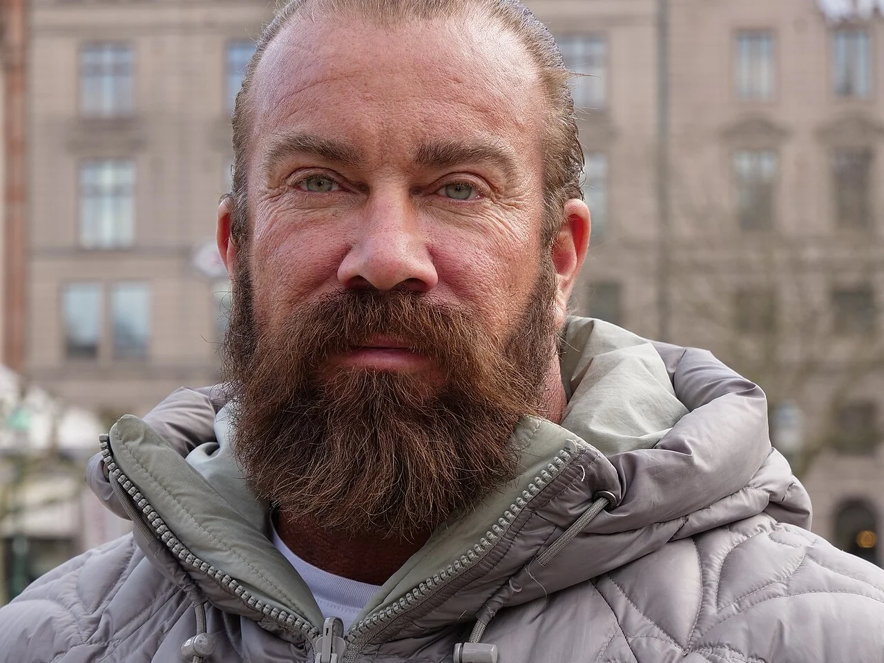 Jan Emanuel med helskägg och grå dunjacka utomhus framför en stenfasad